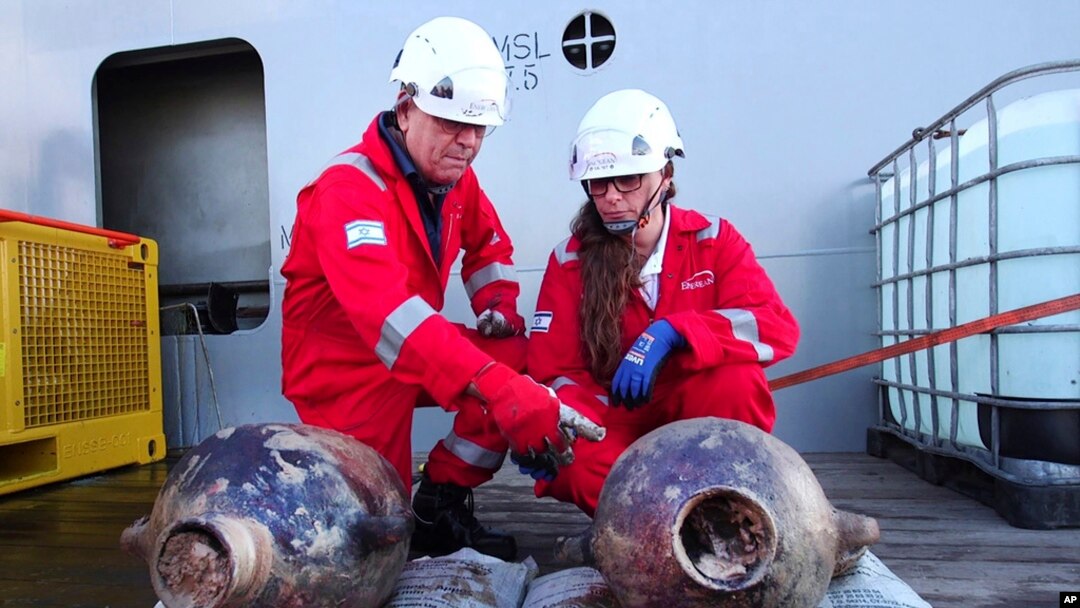 This photo released by Israel's Antiques Authority on June 20, 2024, shows Jacob Sharvit, left, and Dr. Karnit Bahartan with ancient jars that were carried on the world's oldest known deep-sea ship.