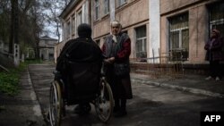 An elderly woman stands beside a man in a wheelchair outside a shelter for internally displaced people, in Dnipro, Ukraine, April 16, 2022.