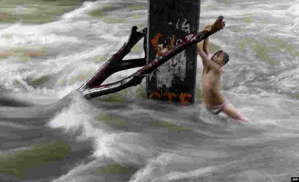 A boy holds a partially submerged tree branch as he plays in a swollen river caused by heavy rains under a bridge in Manila, Philippines.