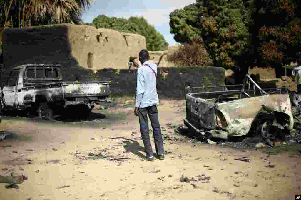 An unidentified man takes a picture of the charred remains of trucks used by radical Islamists on the outskirts of Diabaly, Mali, January 21, 2013.