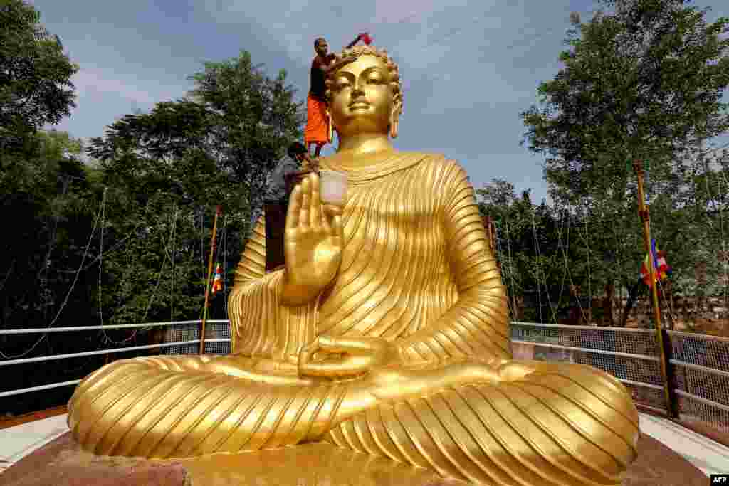 A Buddhist monk climbs atop a giant statue of Buddha to wash and decorate on the eve of Buddha Purnima, a holiday traditionally celebrated for Buddha's birthday also known as Vesak celebrations, in Bhopal, India.