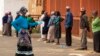 A worker wearing a face mask and gloves to protect herself against coronavirus, joins the queue to receive her social grant outside a pay point in Thokoza, east of Johannesburg, South Africa, March 30, 2020. 