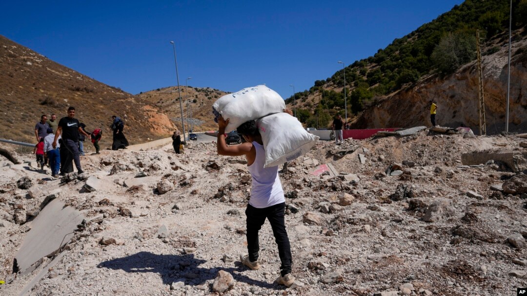 People carry belongings as they cross into Syria on foot through a crater caused by Israeli airstrikes aiming to block Beirut-Damascus highway at the Masnaa crossing, in the eastern Bekaa Valley, Lebanon, Oct. 5, 2024.