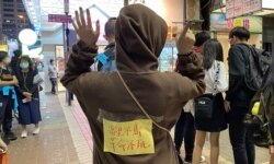 香港市民阿澧11月30日晚在旺角街站写心意卡给12港人，她在背上贴上标语，高举反送中运动”五大诉求、缺一不可”的手势。 (美国之音特约记者汤惠芸摄)