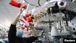 中国浙江湖州一名戴着口罩的工人在生产线上生产出口的袜子。（2020年2月19日）