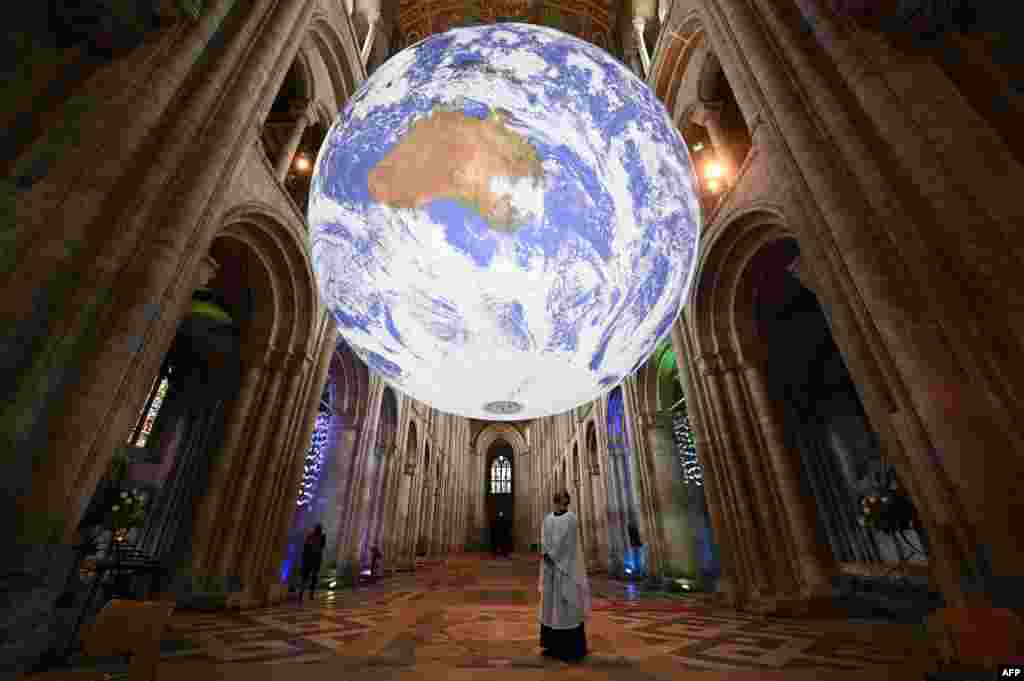 A member of the clergy poses under British artist Luke Jerram's installation 'Gaia', a 7-meter replica of planet Earth, suspended in the nave of Ely Cathedral in Ely, Cambridgeshire, Britain.
