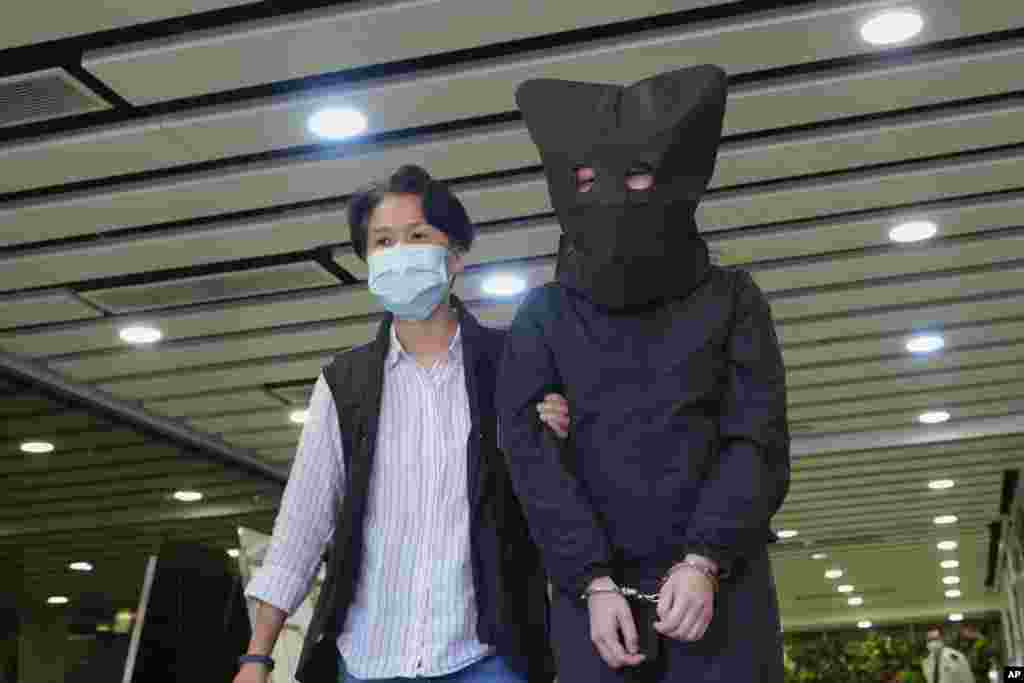 A hooded suspect is accompanied by a police officer to search evidence at office in Hong Kong. National security police arrested five people from a trade union of the General Association of Hong Kong Speech Therapists on suspicion of conspiring to publish and distribute seditious material. 