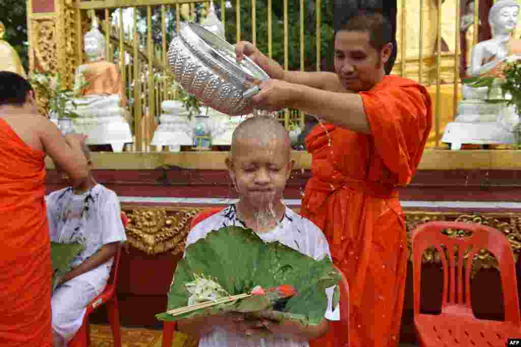 A Buddhist monk bathes the shaved head of the rescued Thai boy and a member of "Wild Boars" football team together with their coach at the Phra That Doi Wao Buddhist temple in the Mae Sai district of Chiang Rai province during the religious ordination ceremony.