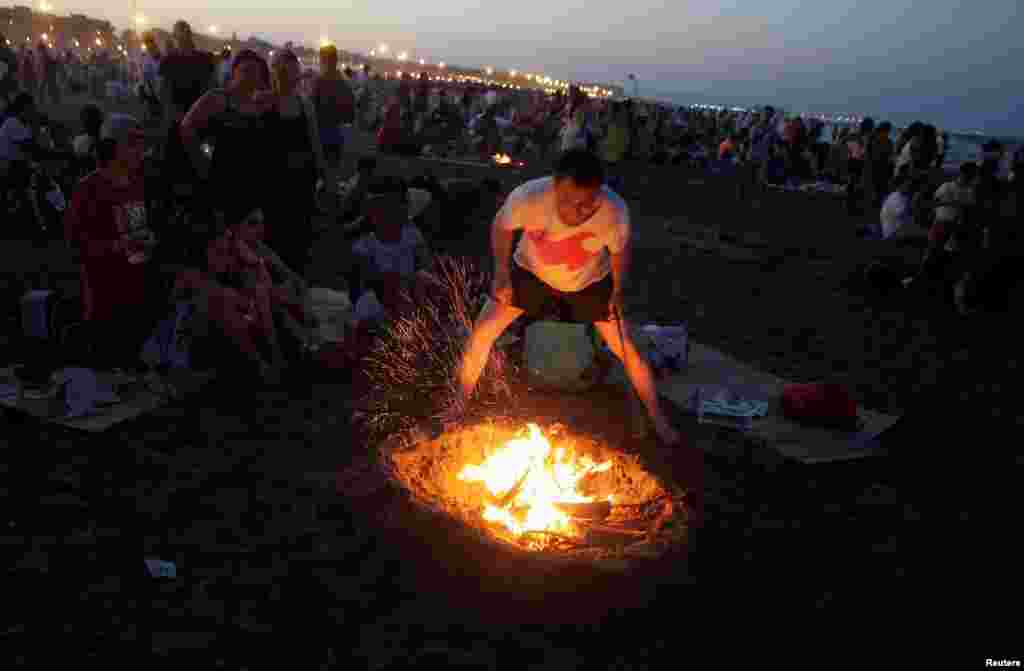 A man tends a bonfire as people gather at the beach to celebrate the summer solstice in Valencia, Spain.