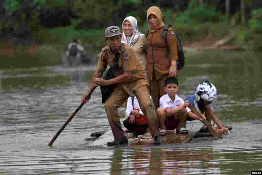A group of teachers and their students use makeshift raft as they cross the flooded street in Ranomeeto Barat village in Konawe Selatan, Sulawesi island, Indonesia.