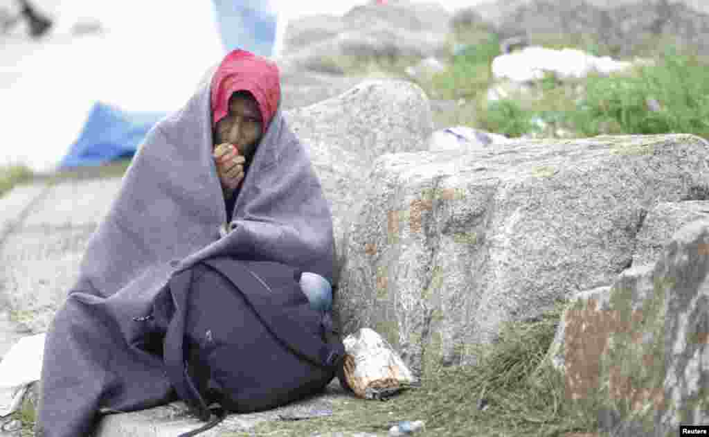 A migrant wrapped in a blanket eats an apple in a make-shift camp at the border crossing in Nickelsdorf, Austria, Sept. 6, 2015.