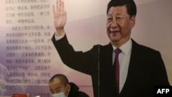 中國遼寧省瀋陽市的一家書店裡一名戴著口罩的讀者坐在中國國家領導人習近平的大幅畫像前。（2020年4月23日）