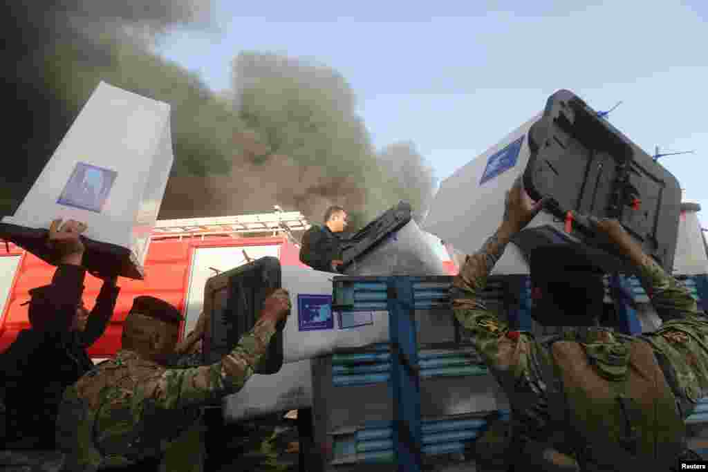 Security forces carry ballot boxes as smoke rises from a storage site housing the boxes from Iraq's May parliamentary election, in Baghdad, June 10, 2018.