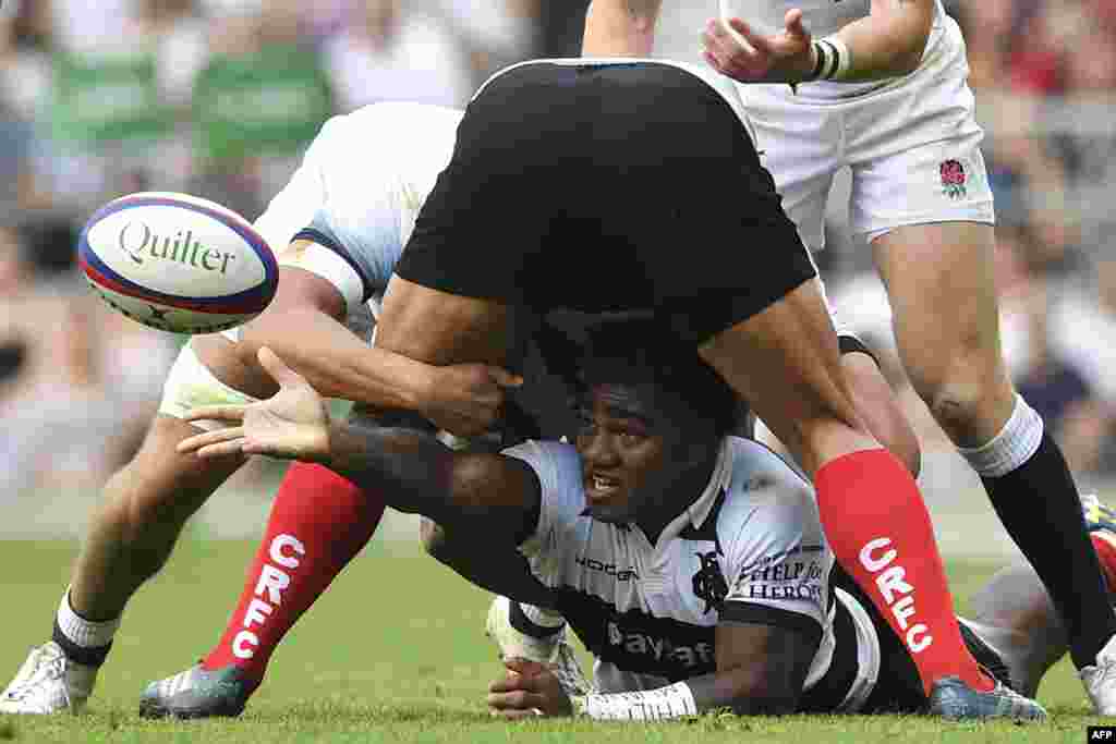 Barbarians' Fijian wing Josua Tuisova (C) passes the ball from the floor during the international friendly rugby union match between England and the Barbarians at the Twickenham, west London.