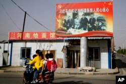 2018年9月20日新疆地区一维吾尔族妇女载着学童走过一张中国国家主席习近平与一群维吾尔族老人手牵手的照片