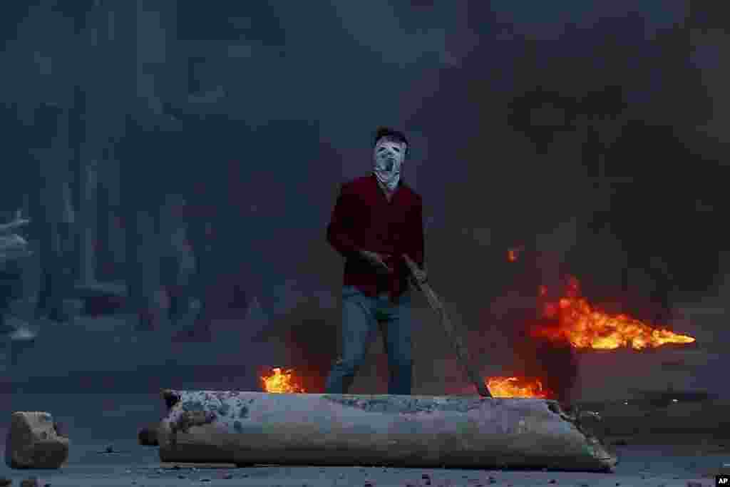 A masked Kashmiri protester watches from a distance as Indian policemen fire tear gas shells towards him during a protest in Srinagar, Indian controlled Kashmir.