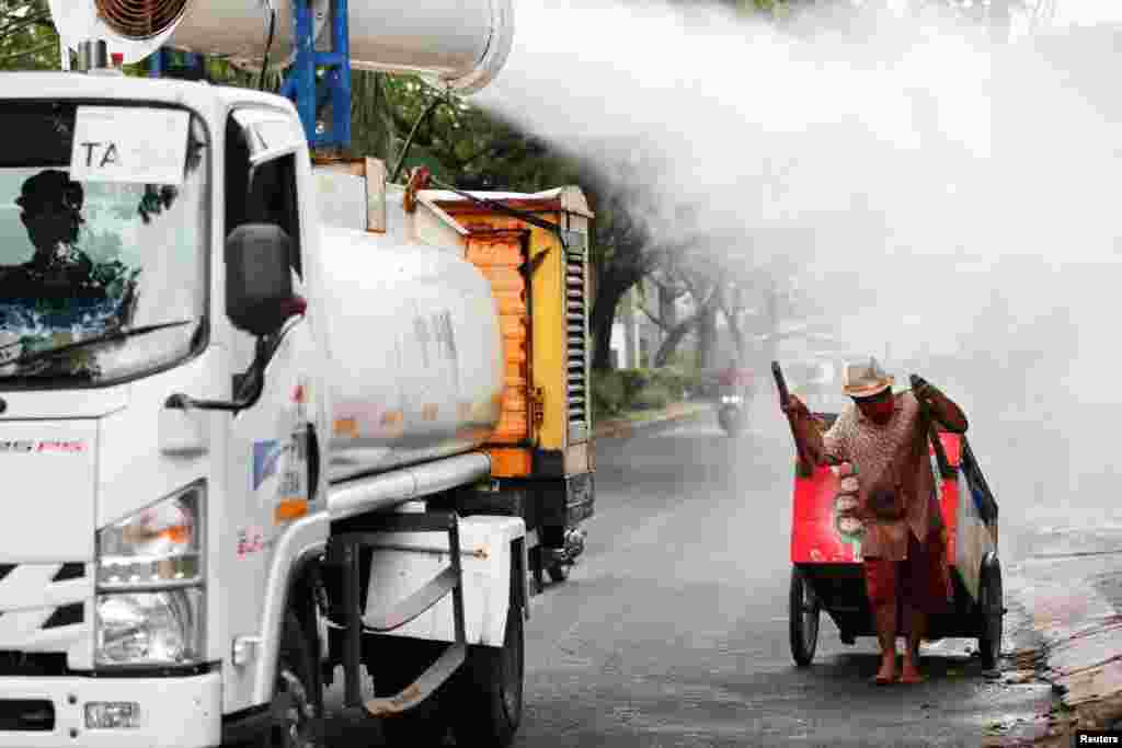 A man pulling a cart reacts as Indonesian Red Cross personnel spray disinfectant using a gunner around the Daan Mogot neighborhood as the COVID-19 cases surge in Jakarta, Indonesia.