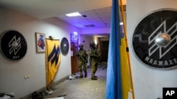 Російські солдати проходять по базі українського полку «Азов», прикрашеній емблемами підрозділу.