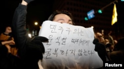 2024年12月4日，韩国总统尹锡烈宣布戒严后，人们聚集在首尔国会大厦，一个人举着一块写着“民主不会向尹锡烈屈服”字样的标语牌。