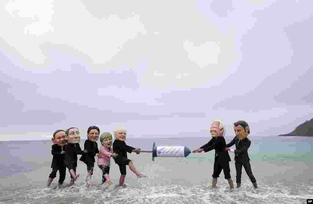 Activists wearing giant heads of the G7 leaders tussle over a giant COVID-19 vaccine syringe during an action of NGO's on Swanpool Beach in Falmouth, Cornwall, England.