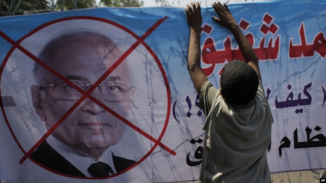 An Egyptian youth hangs a banner with a defaced picture of presidential candidate, Ahmed Shafiq and Arabic that reads "Shafiq, the former regime," during a protest in front the Supreme Constitutional Court in Cairo, Egypt, June 14, 2012.