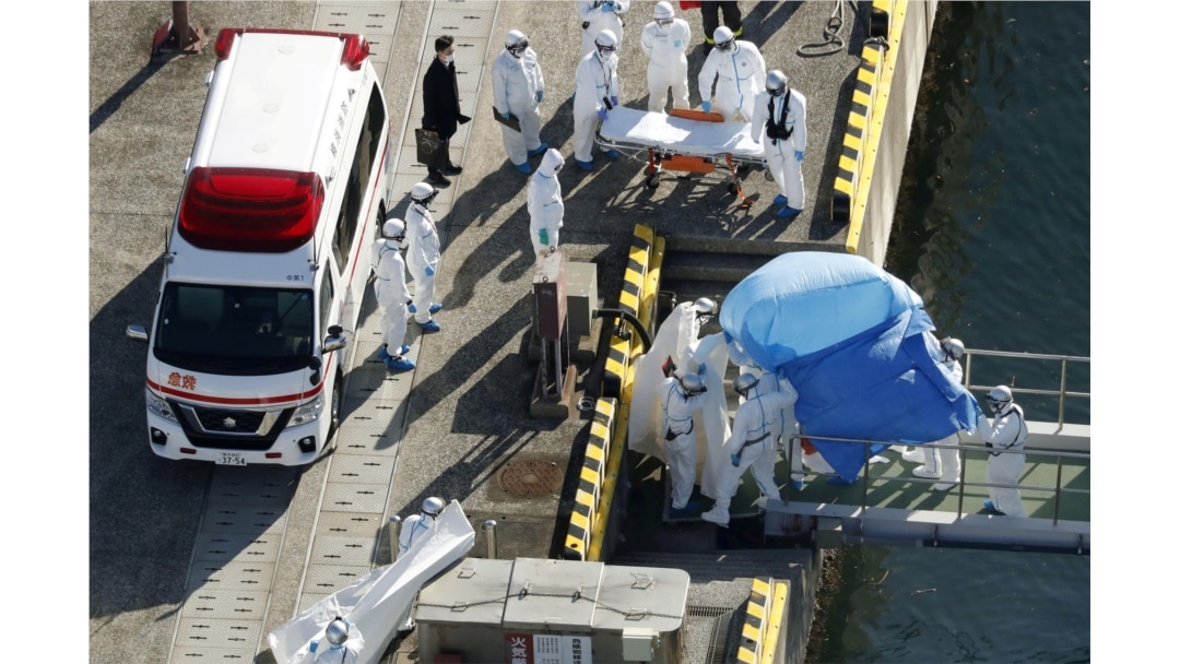 Officers in protective gear escort a person (under the blue sheet) who was on board cruise ship Diamond Princess and was tested positive for coronavirus, in Yokohama, south of Tokyo in this photo taken by Kyodo, Feb. 4, 2020.