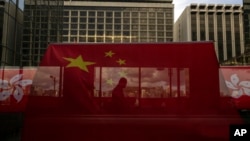 资料照：香港主权移交26周年纪念期间，中国国旗和香港区旗高挂香港街道大楼，旗帜后有行人走过天桥。（美联社，2023年6月27日）