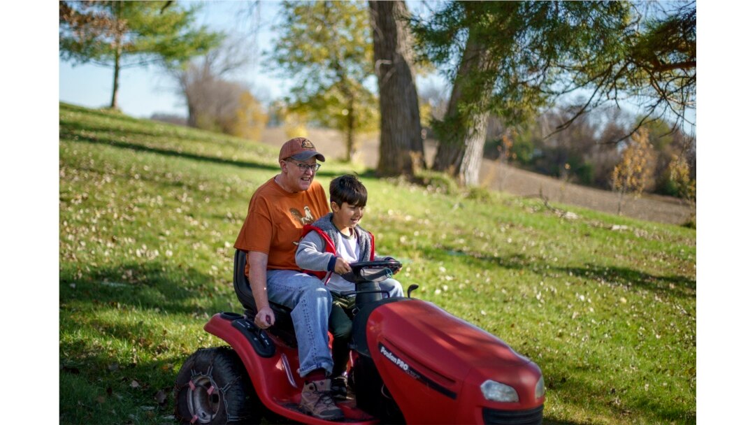 Caroline Clarin rides with Ali Patan, 7, as he drives her riding mower at her home in Dalton, Minn., Oct. 30, 2021.