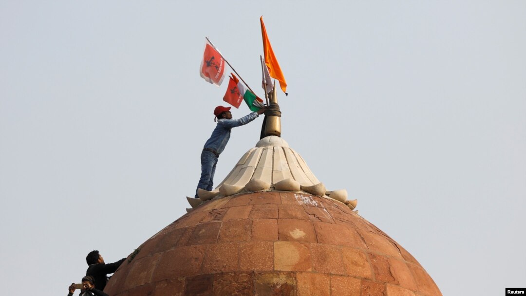A man holds a flag as he stands on the top of the historic Red Fort during a protest against farm laws introduced by the government, in Delhi, India, Jan. 26, 2021. 