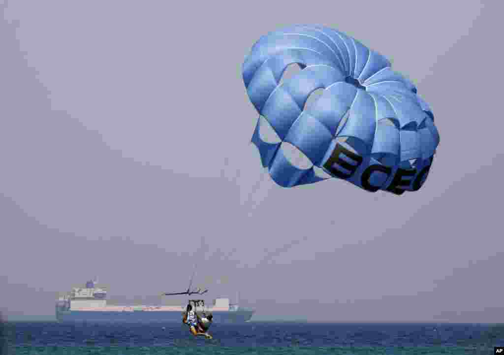 Holidaymakers parasail as a cargo ship crosses the Gulf of Suez towards the Red Sea at El Sokhna beach in Suez, Egypt.