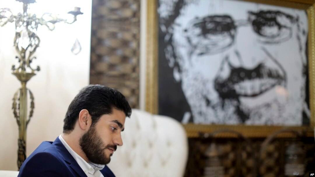 FILE - Abdullah Morsi, the youngest son of Egypt's former President Mohamed Morsi, sits in front of a framed image of his father that was printed on a flag during the 2013 Rabaah al-Adawiya sit-in, at his home in Cairo, Egypt.
