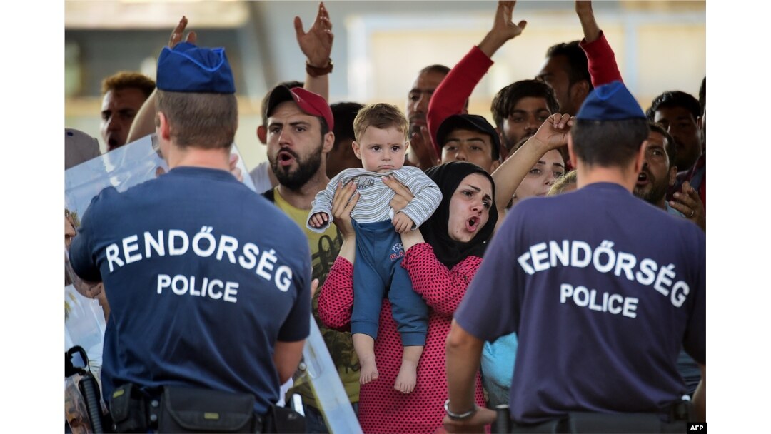 Hungarian police officers face a group of Syrian migrants, with a woman holding a baby, on the platform of the Kobanya-Kispest station, Budapest suburb, on Sept. 2, 2015, as the refugees refused to board a train to the Debrecen camp.