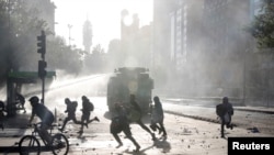 People and demonstrators run as a riot police vehicle uses a water cannon during a protest against Chile's government in Santiago, Chile, Oct. 29, 2019.