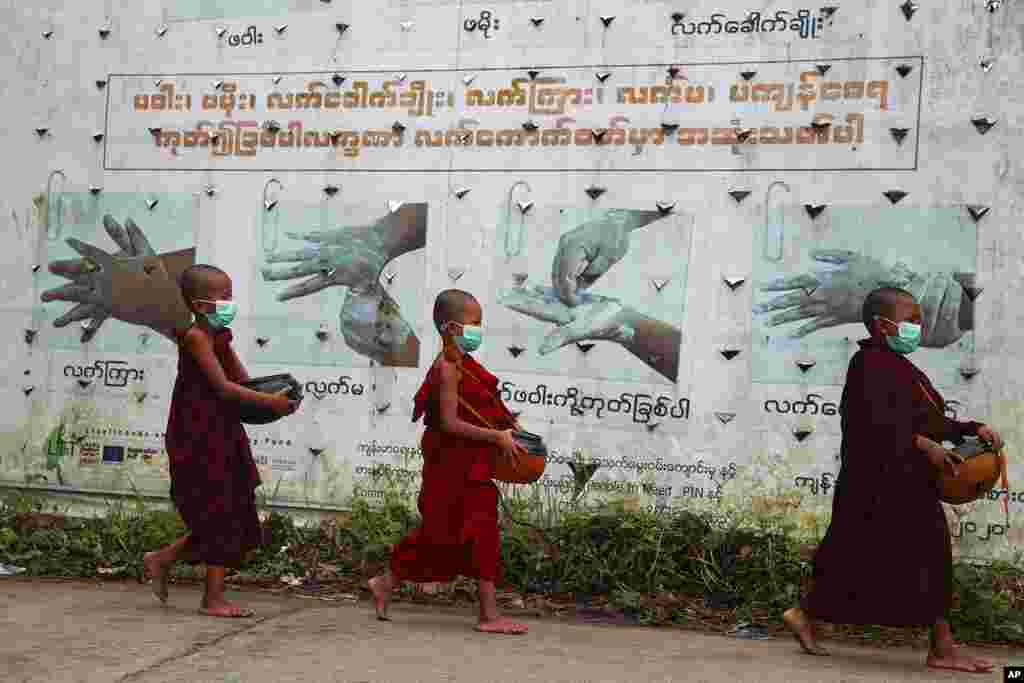 Buddhist novice monks wearing face masks walk past a COVID-19 awareness sign as they collect morning alms, in Yangon, Myanmar.