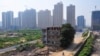 FILE - A man rides his bicycle past a partially demolished building in the middle of a street next to new residential construction sites in Xi'an, August 14, 2013.