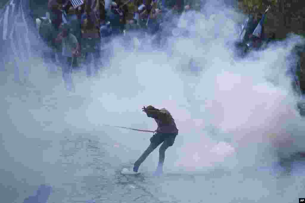 An opponent of the deal between Greece and Macedonia kicks a tear gas thrown by riot police during clashes at the village of Pisoderi near the border with Macedonia in northern Greece. The foreign ministers of Greece and Macedonia signed a preliminary accord to end a decade-long dispute by renaming Macedonia the Republic of North Macedonia. 