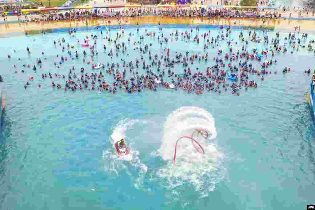 People watch a flyboard performance as they cool off in a swimming pool in Lianyungang, in China's eastern Jiangsu province, July 4, 2021.