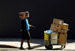 FILE - In this Oct. 1, 2020, photo an Amazon worker wears a mask and gloves as he delivers boxes downtown Los Angeles.