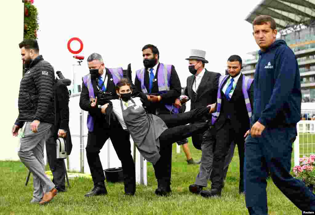 An extinction rebellion protester is escorted from the racecourse during the Royal Ascot horse race in Ascot, England, June 19, 2021.