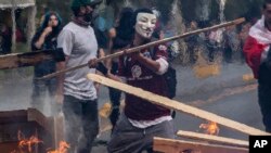 A demonstrator wearing a mask throws a plank of wood into a flaming barricade during protests in Santiago, Chile, Oct. 19, 2019. 