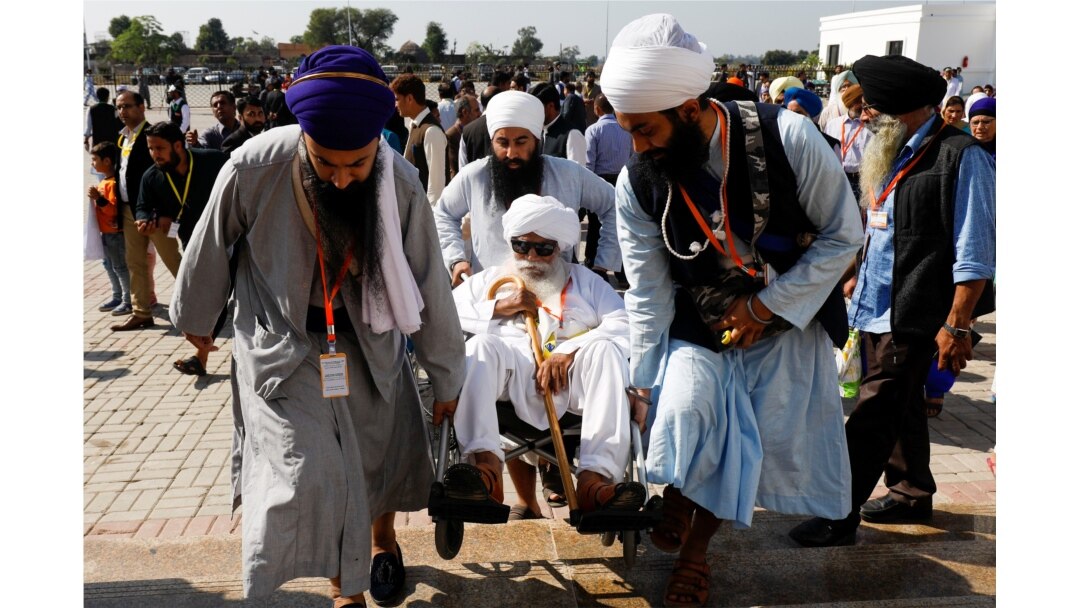 Indian Sikh pilgrims help a man on a wheelchair as they visit the Gurdwara Darbar Sahib, in Kartarpur, Pakistan, Nov. 9, 2019.