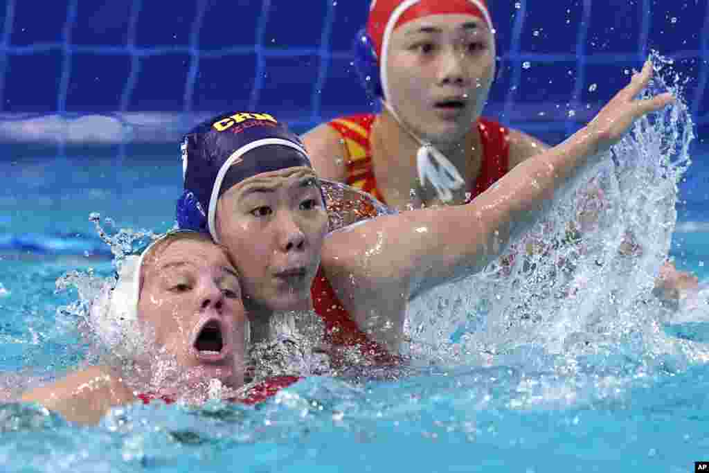Hungary's Aniko Gyongyossy, left, and China's Wang Huan battle for position in front of China's goalkeeper Shen Yineng, right, during a preliminary round women's water polo match at the 2020 Summer Olympics in Tokyo, Japan.