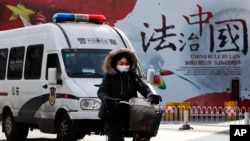 A woman and a police van pass a Chinese government propaganda billboard that reads "China Rule By Law" on a street in Beijing, Dec. 28, 2016. Many in China are infuriated by a decision to drop charges in a high-profile police brutality case.