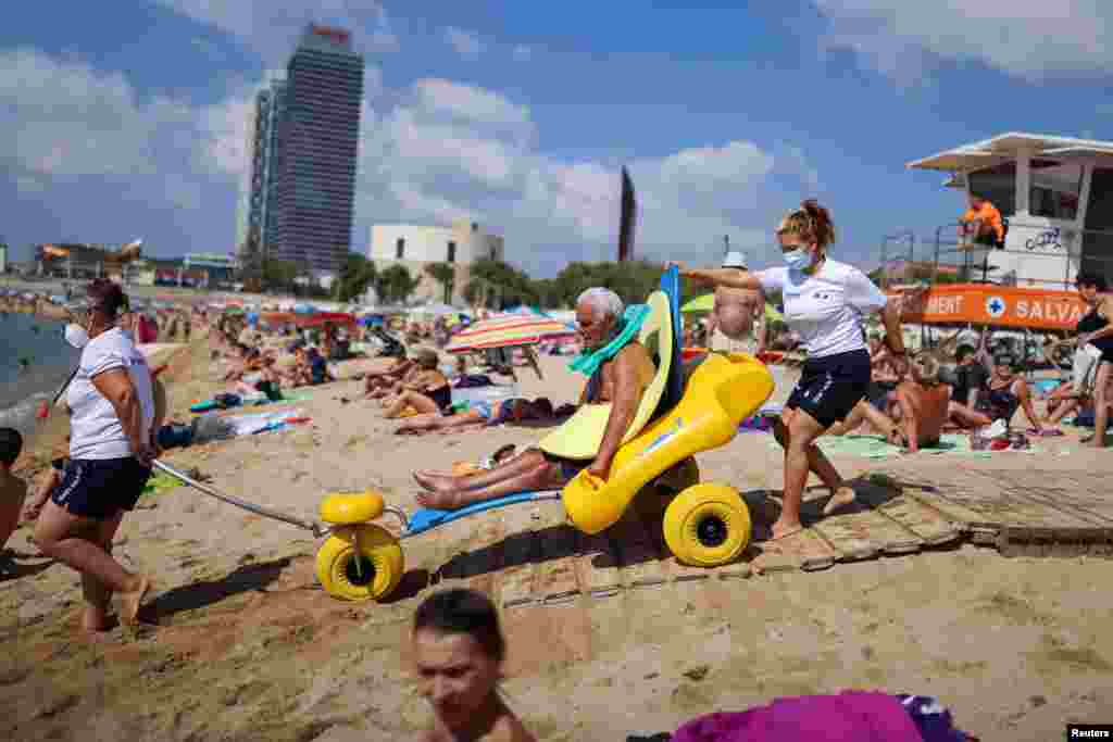 Disabled Manuel Molina, 80, sits on an amphibious chair as he is helped by lifeguards Olga Diaz and Micaela before swimming in the Mediterranean sea, on Barcelona's Nova Icaria Beach, Spain.